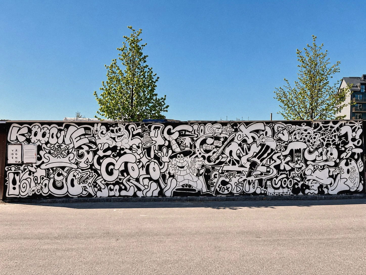 Lång svartvit mural med täta, slingrande figurer och mönster på en vägg under blå himmel